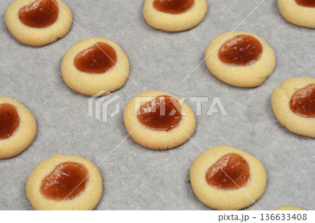 Baked thumbprint cookies with jam filling on baking paper Baked thumbprint cookies with jam filling on baking paper 136633408