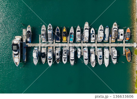 Aerial view of luxury yachts docked at marina. Top-down drone shot of yachts. Boats and sailboats line the scenic seashore. Aerial view of luxury yachts docked at marina. Top-down drone shot of yachts. Boats and sailboats line the scenic seashore. 136633606