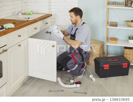 Man plumber in uniform with toolbox replacing the water filter or fixing broken pipe in kitchen. 136633695