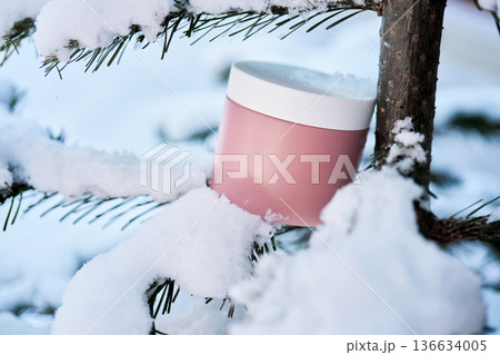 Pink skincare jar in snow on pine branch 136634005