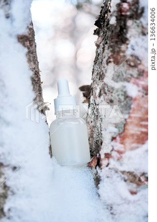 Skincare serum bottle standing in snow on birch tree Skincare serum bottle standing in snow on birch tree 136634006