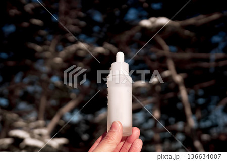 Hand holding dropper bottle with skincare product in winter Hand holding dropper bottle with skincare product in winter 136634007
