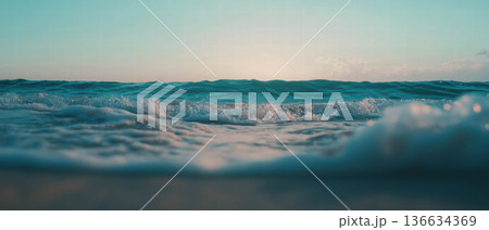 Soft waves gently lap against a tranquil sandy beach, creating a serene atmosphere. 136634369
