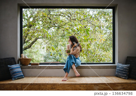 Beautiful woman sitting in front of large window, drinking tea. Beautiful woman sitting in front of large window, drinking tea. 136634798