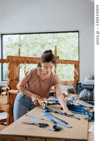 Young businesswoman working on workbench, preparing old fabric for weaving. 136634804