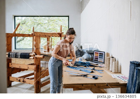 Young businesswoman working on workbench, preparing old fabric for weaving. Young businesswoman working on workbench, preparing old fabric for weaving. 136634805