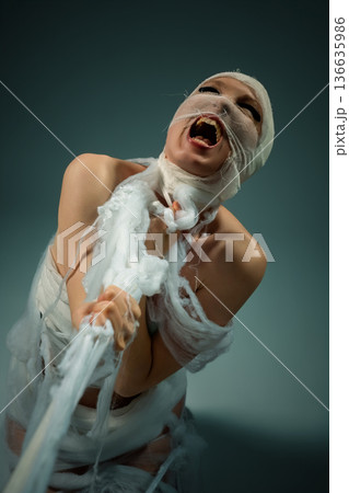 Person wrapped in white bandages screaming in anguish and struggling to break free. 136635986