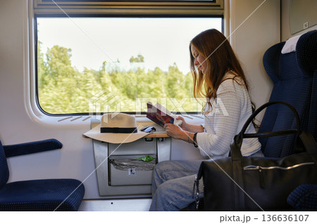 Woman reading book by train window with green landscape 136636107