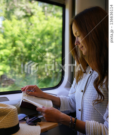 Woman reading book by train window in summer countryside Woman reading book by train window in summer countryside 136636114