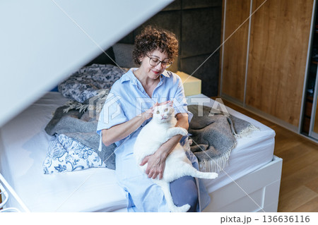 tender calm mood, glasses, woman sitting on bed, petting white cat on lap, relaxed home atmosphere, cozy bedroom, soft textiles, White, forties, emotional comfort, quiet companionship tender calm mood, glasses, woman sitting on bed, petting white cat on lap, relaxed home atmosphere, cozy bedroom, soft textiles, White, forties, emotional comfort, quiet companionship 136636116