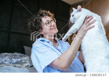 joyful playful mood, glasses, smiling woman holding large white cat, pet bonding, home bedroom, soft morning light, cozy weekend moment, White, forties, animal care, affectionate interaction joyful playful mood, glasses, smiling woman holding large white cat, pet bonding, home bedroom, soft morning light, cozy weekend moment, White, forties, animal care, affectionate interaction 136636117