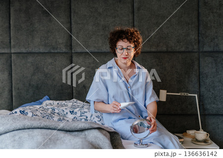 A woman in a blue armchair relaxes at home, reading a book and stroking her white cat. Concept of animal companionship, domestic peace, mindfulness, and slow living during a quiet weekend. 136636142