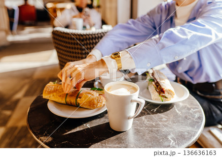 Close-up of woman hands reaching for fresh sandwich on marble cafe table with coffee cup. Real life breakfast moment, urban coffee culture, slow living, casual lifestyle, authentic everyday food 136636163