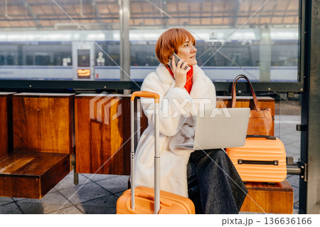 Thoughtful middle aged woman sitting on bench with laptop suitcase at railway station platform. Experienced professional reflecting, planning tasks transit, independence decision making in modern city 136636166