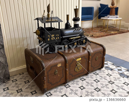 Vintage train model on old suitcase in modern interior. Conveys nostalgia, decor, and the fusion of historical objects within contemporary design aesthetics. Vintage train model on old suitcase in modern interior. Conveys nostalgia, decor, and the fusion of historical objects within contemporary design aesthetics. 136636660
