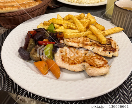 Grilled chicken with fries and vegetables on restaurant table. Conveys balance, nourishment, and a casual dining experience with focus on food and togetherness. Grilled chicken with fries and vegetables on restaurant table. Conveys balance, nourishment, and a casual dining experience with focus on food and togetherness. 136636661