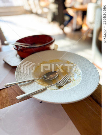 Empty plate with fork and spoon after meal in restaurant. Represents satisfaction, appetite, and the quiet moment after a delicious dining experience. Empty plate with fork and spoon after meal in restaurant. Represents satisfaction, appetite, and the quiet moment after a delicious dining experience. 136636666