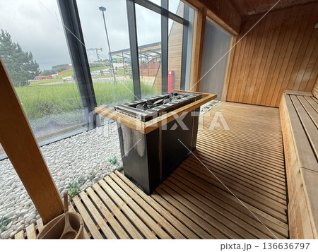 Sauna heater with stones near glass wall and pebble bed. Heat therapy, wellness ritual, relaxation practice, detox process, hygiene tradition Sauna heater with stones near glass wall and pebble bed. Heat therapy, wellness ritual, relaxation practice, detox process, hygiene tradition 136636797
