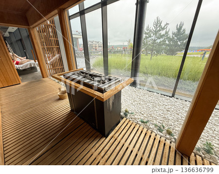 Sauna heater with stones near glass wall and pebble bed. Heat therapy, wellness ritual, relaxation practice, detox process, hygiene tradition Sauna heater with stones near glass wall and pebble bed. Heat therapy, wellness ritual, relaxation practice, detox process, hygiene tradition 136636799