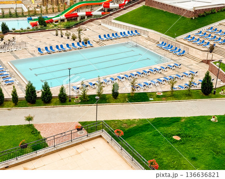 Waterpark with pools, colorful slides, and sunbeds surrounded by hills and countryside landscape. Tourism, leisure, and recreation symbolizing summer activity, entertainment, and vacation lifestyle. Waterpark with pools, colorful slides, and sunbeds surrounded by hills and countryside landscape. Tourism, leisure, and recreation symbolizing summer activity, entertainment, and vacation lifestyle. 136636821