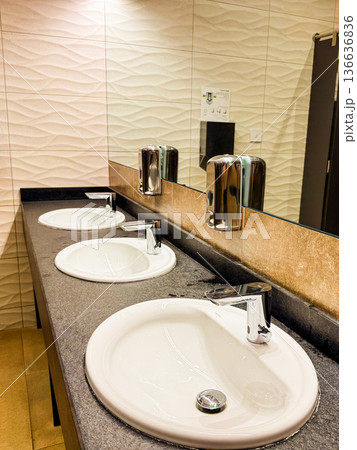 Triple sink counter with mirror and tiled wall in modern restroom. Cleanliness, hygiene, and functional hospitality facility for comfort, order, and guest service. Triple sink counter with mirror and tiled wall in modern restroom. Cleanliness, hygiene, and functional hospitality facility for comfort, order, and guest service. 136636836