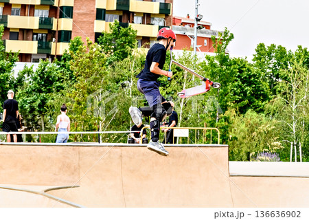 Young man practicing Scootering (Freestyle Scootering) in the new SkatePark in the central park of Igualada, Barcelona, Spain. 136636902