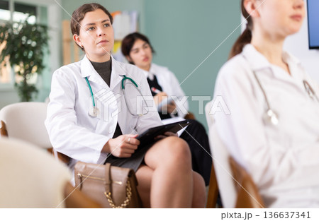 Young girl medical student dressed in labcoat sitting and listening lecture, taking notes on tablet in lecture hall 136637341