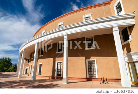 New Mexico State Capitol in Santa Fe. Unique Roundhouse architecture features a curved adobe facade with white columns and trim under a blue sky New Mexico State Capitol in Santa Fe. Unique Roundhouse architecture features a curved adobe facade with white columns and trim under a blue sky 136637816