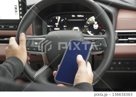 運転席でスマホを操作している男性の手元 136638363