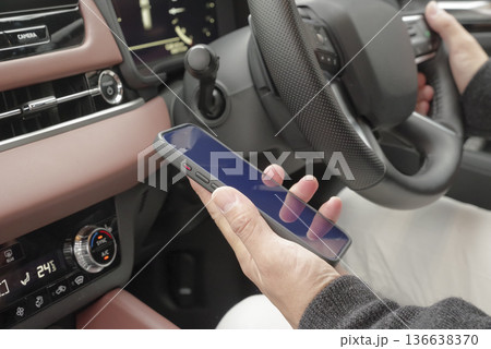 運転席でスマホを操作している男性の手元 136638370