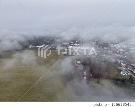 Townscape Veiled Behind Drifting Mist And Clouds, Misty Urban Setting With Rooftops And Winding Roads Visible 136638549