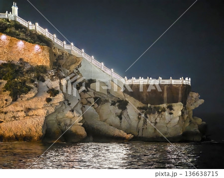 Serene Waterside Viewing Path, Calm Ocean Reflections From Illuminated Cliffside Walkway At Night 136638715