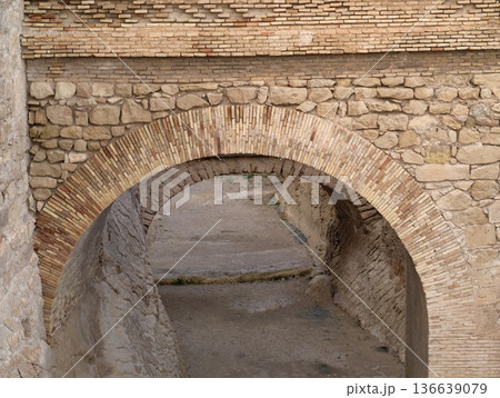 Weathered Stone Arch Over Dry Waterway, Old Masonry Bridge With Moss And Layered Sandstone Surfaces 136639079