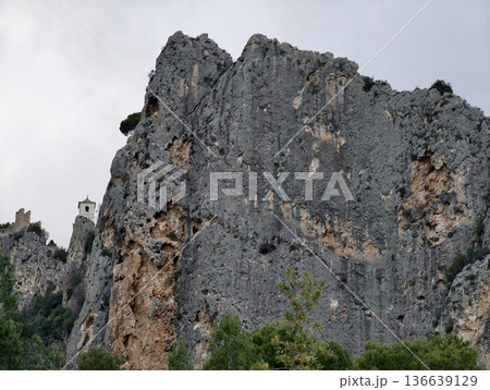 Steep And Dramatic Rocky Cliff Rising Above Dense Pine Bush Under Ominous Weather Conditions Steep And Dramatic Rocky Cliff Rising Above Dense Pine Bush Under Ominous Weather Conditions 136639129
