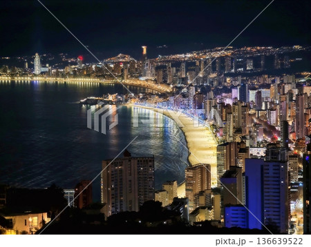 Bright Coastal City From Above, Skyline Illuminated At Night With Winding Streets And Distant Lights Bright Coastal City From Above, Skyline Illuminated At Night With Winding Streets And Distant Lights 136639522