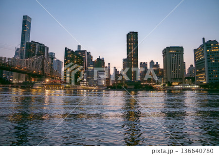 The Manhattan skyline and Queensboro Bridge glow with city lights, mirrored in the rippling East River. The sky transitions from soft blue to warm tones as the city settles into night. The Manhattan skyline and Queensboro Bridge glow with city lights, mirrored in the rippling East River. The sky transitions from soft blue to warm tones as the city settles into night. 136640780
