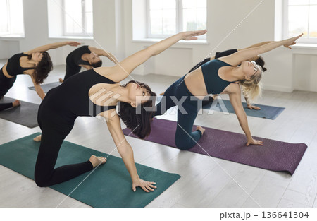 Dynamic yoga class performing side-bending poses on mats in a bright studio 136641304