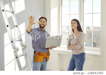 Happy worker with laptop talking to young woman about repairs and renovations in her house 136641305