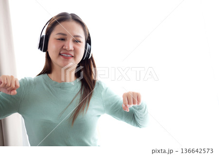 Happy young asian woman wearing headphones listening music while standing dancing with fun. Happy young asian woman wearing headphones listening music while standing dancing with fun. 136642573