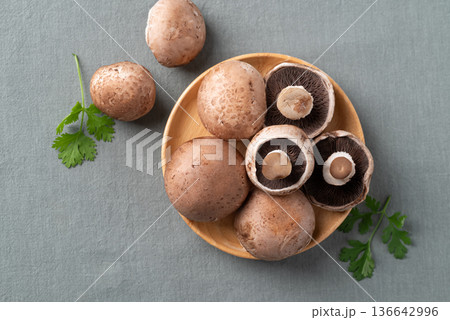 Top view of fresh crimini mushroom or baby bella mushroom on wooden plate with fabric background Top view of fresh crimini mushroom or baby bella mushroom on wooden plate with fabric background 136642996
