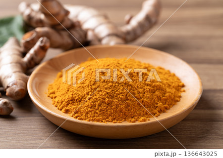 Turmeric powder in a wooden bowl with fresh roots on a wooden background. Organic healthy spice Turmeric powder in a wooden bowl with fresh roots on a wooden background. Organic healthy spice 136643025