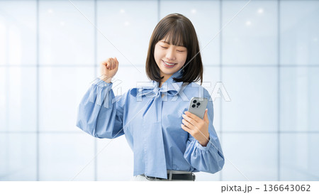 スマートフォンを見てガッツポーズをする若い女性・ビジネスウーマン 136643062