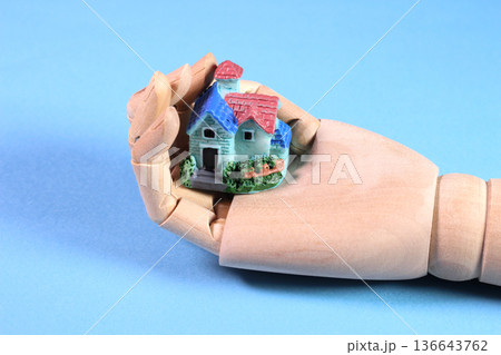ウッドハンドの上に載ったミニチュアハウス 水色背景（不動産・マイホームのイメージ） 136643762