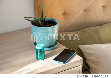 Medicine bottle with pills, plant and smartphone on nightstand for healthcare. Medicine bottle with pills, plant and smartphone on nightstand for healthcare. 136644011