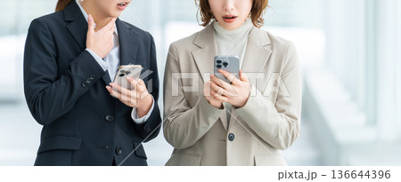 スマートフォンを見て驚く2人の女性・ビジネスウーマン スマートフォンを見て驚く2人の女性・ビジネスウーマン 136644396