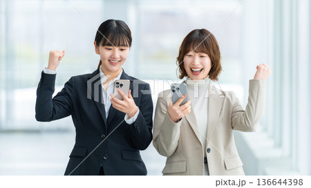 スマートフォンを見てガッツポーズで喜ぶ2人の女性・ビジネスウーマン 136644398