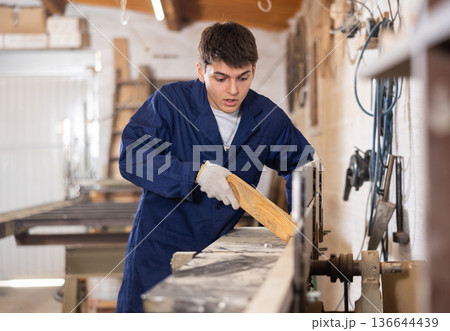 Young man cutting wooden board with circular saw at sawmill 136644439