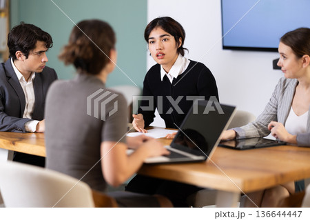 Interested office workers sitting at table with papers and laptop and discussing ideas during business meeting in office 136644447
