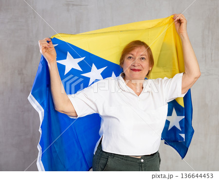 Smiling senior lady waving flag of Bosnia and Herzegovina Smiling senior lady waving flag of Bosnia and Herzegovina 136644453