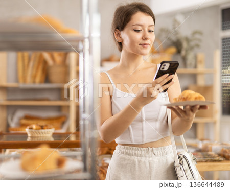 Female customer scanning QR code on label of fresh baked goods in bakery interior Female customer scanning QR code on label of fresh baked goods in bakery interior 136644489